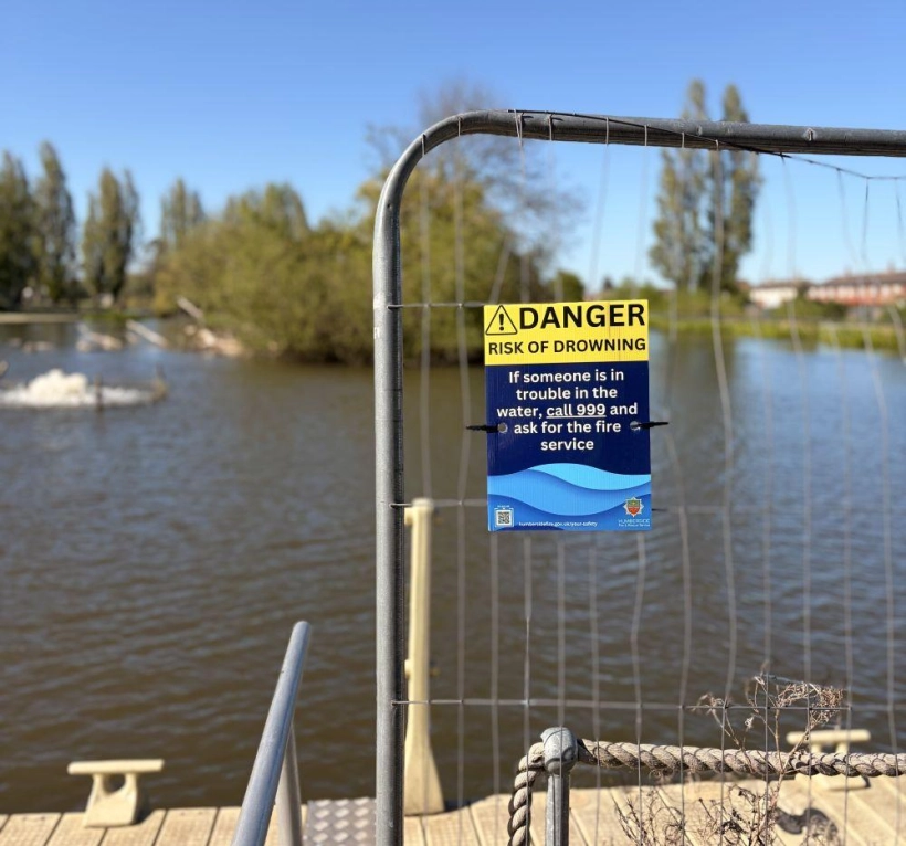 Water safety sign on metal fencing around a lake